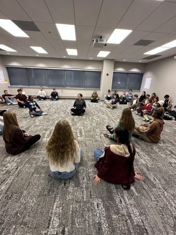 Students participate in a listening activity while sitting cross legged on the floor.